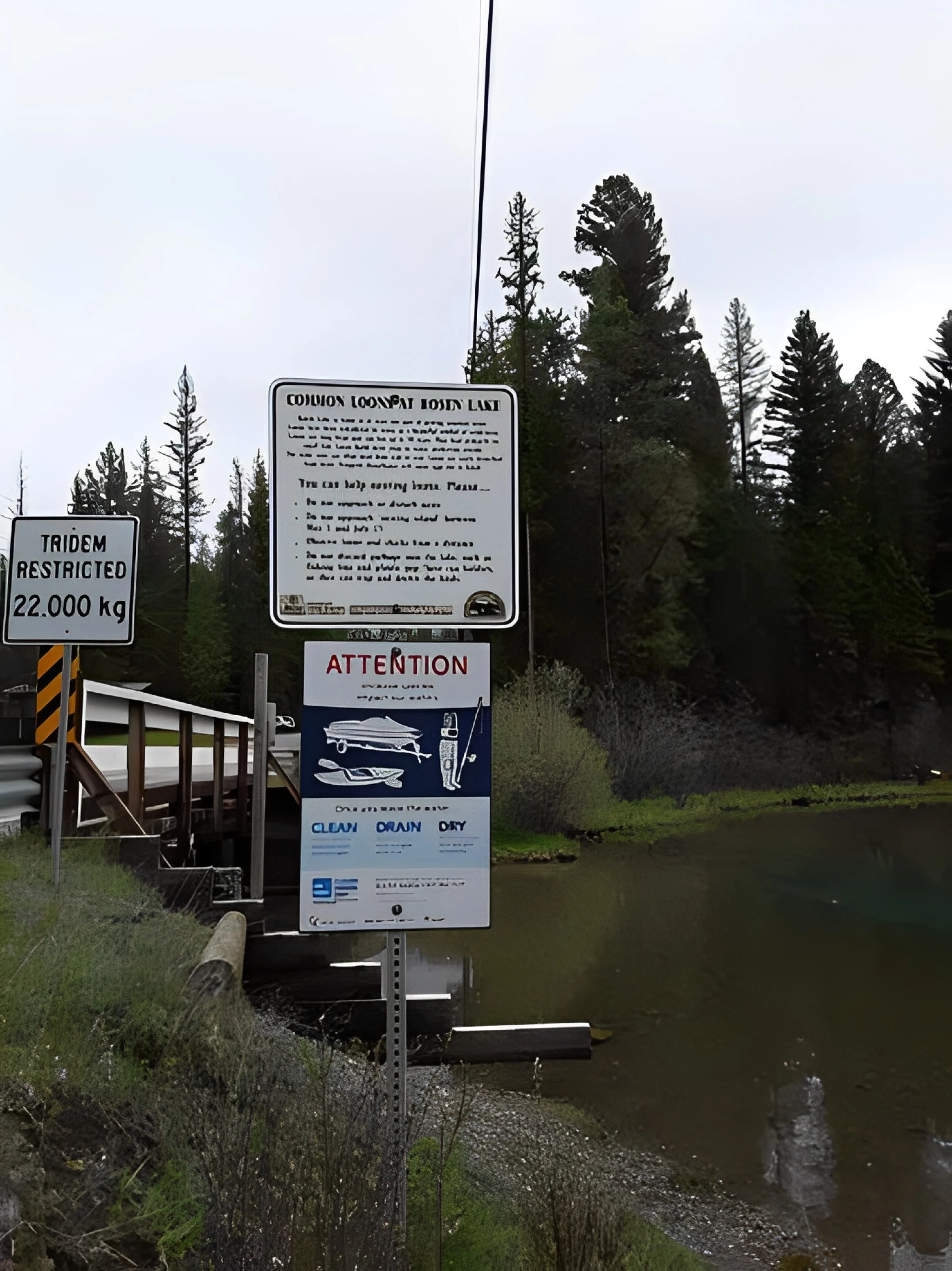 A sign on the side of a river near trees.